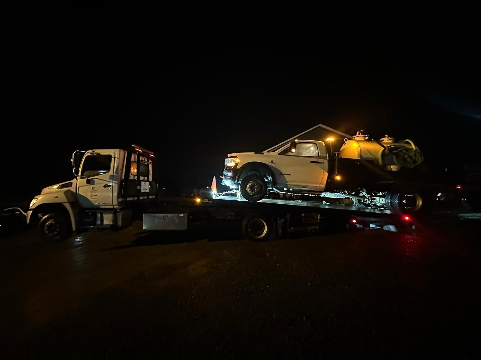 Tow truck hauling a silver car loaded with debris at night on a dark road