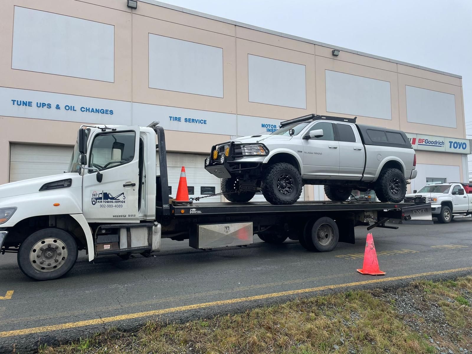 Tow truck hauling a silver pickup with front-end damage on a city street