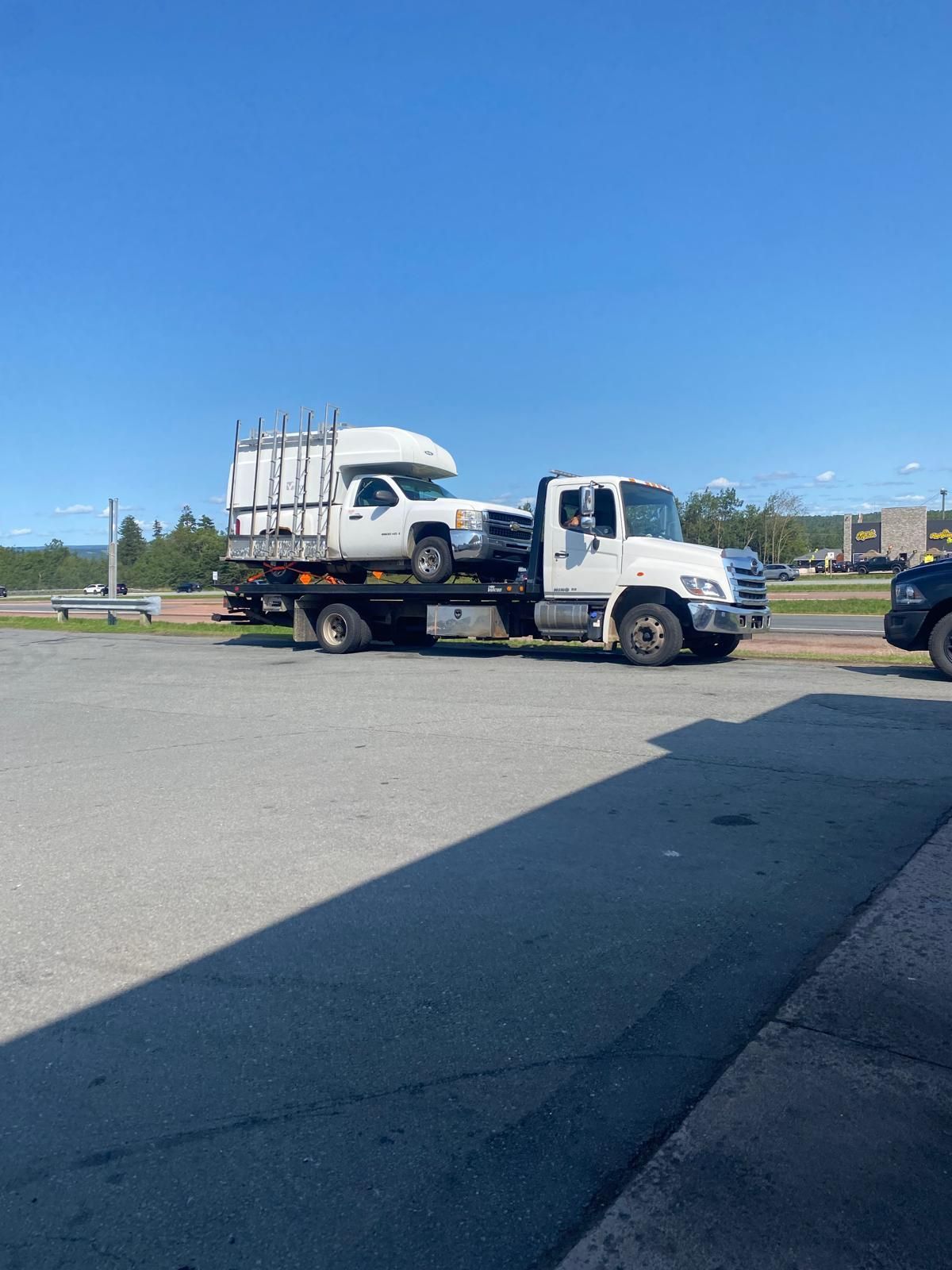 Tow truck carrying a white pickup in a parking lot under a clear blue sky