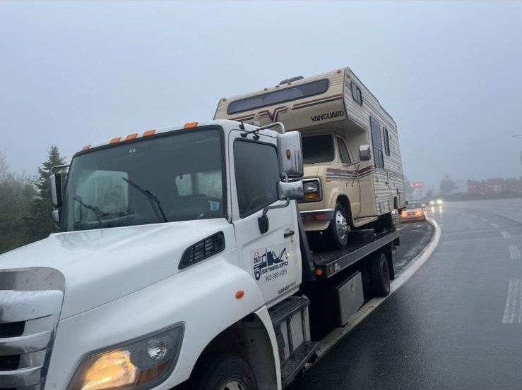 Tow truck hauling a beige RV on a foggy, wet highway curve