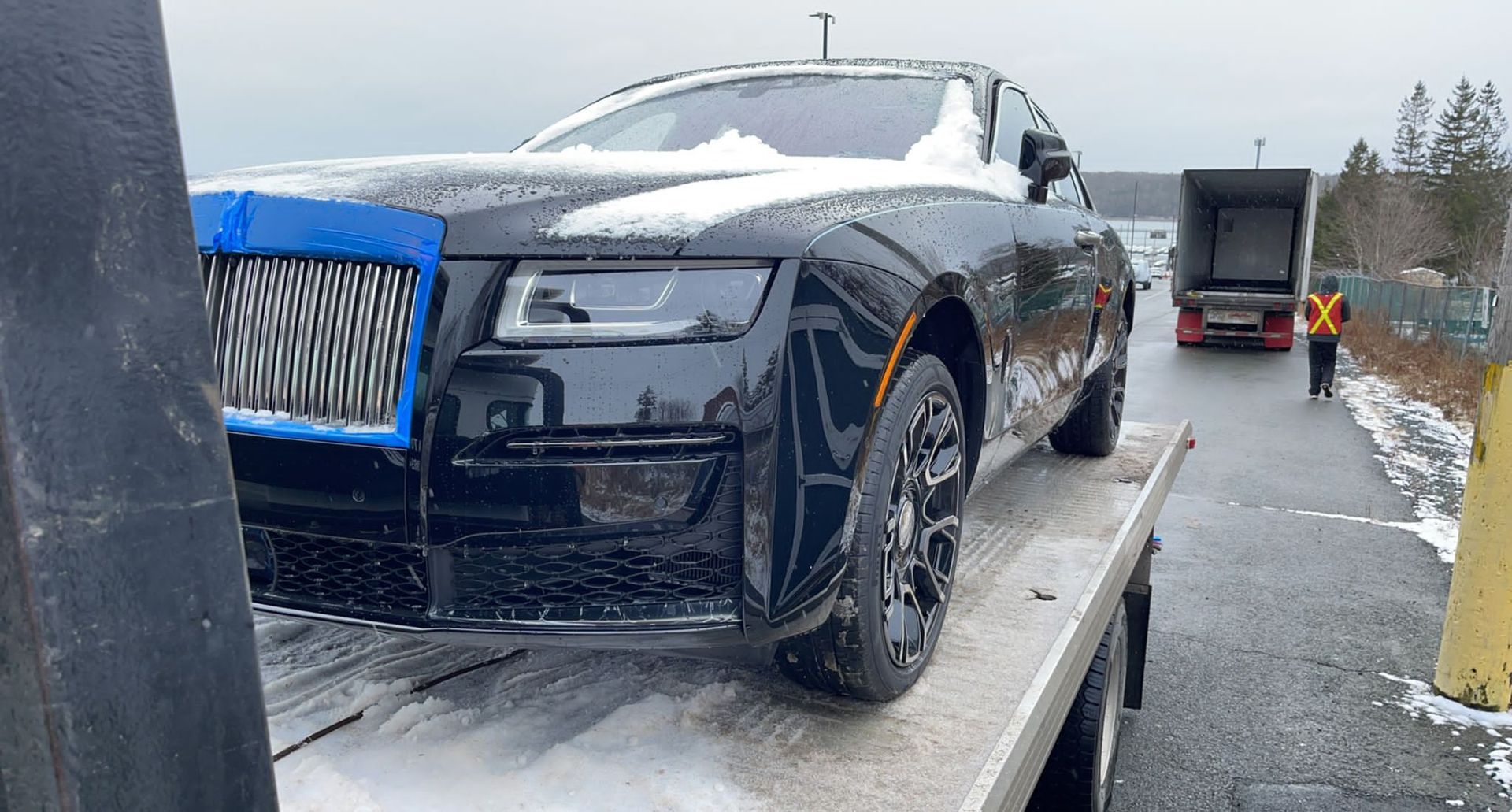 Black luxury sedan on a tow truck in a snowy roadside scene