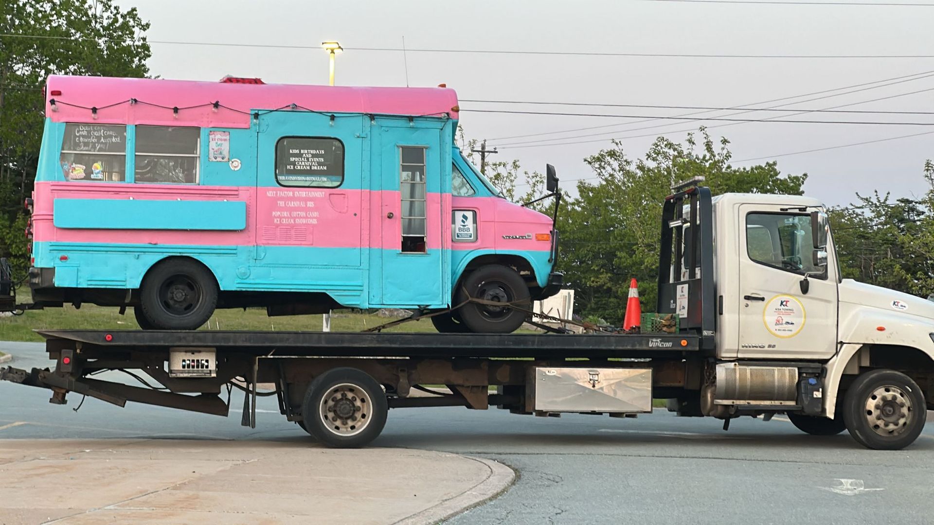 Tow truck hauling a pink and turquoise food truck on a flatbed