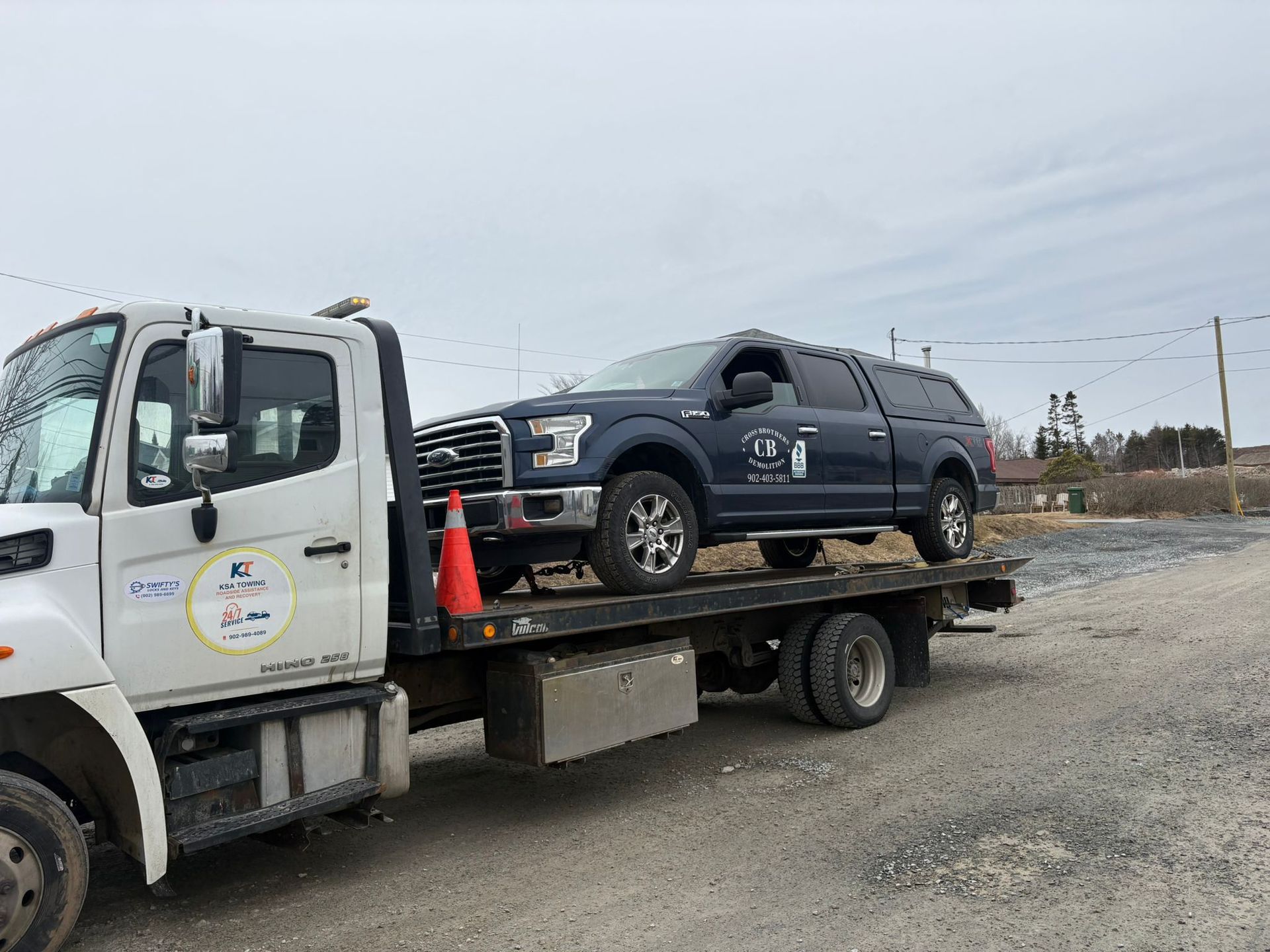 Tow truck hauling a dark SUV on a flatbed near orange cones in a gravel lot