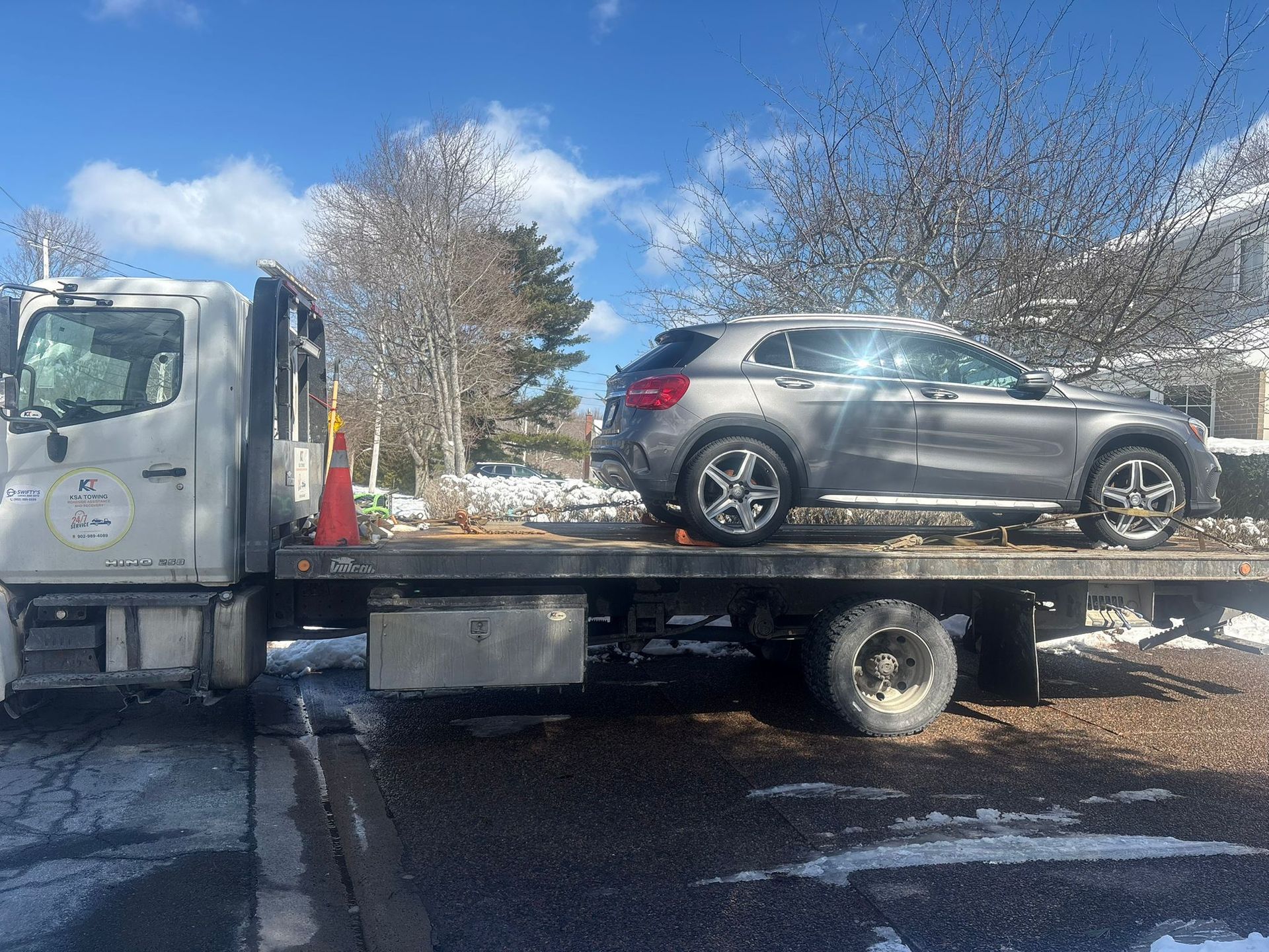 Tow truck hauling a silver SUV on a flatbed in a snowy parking lot