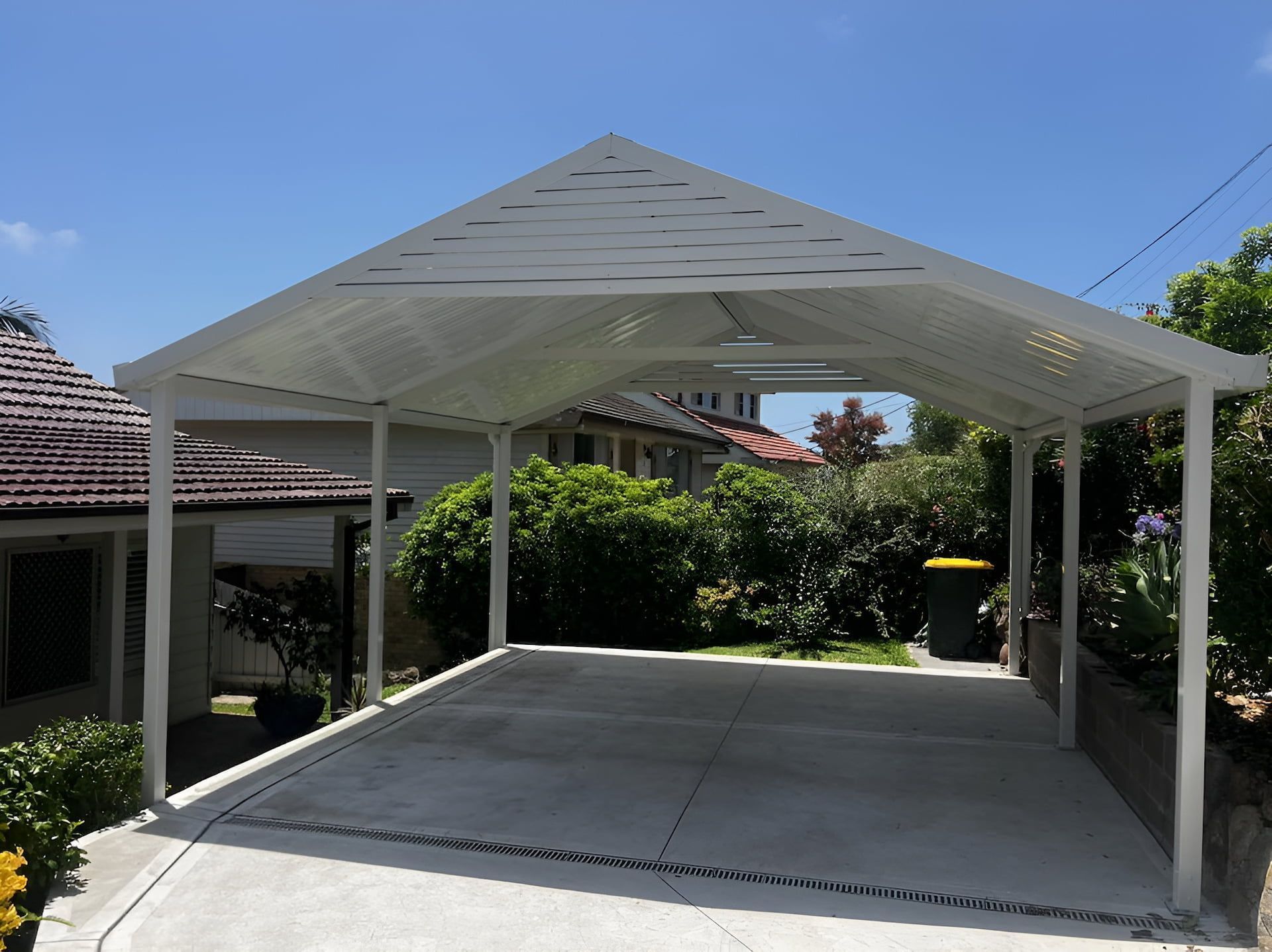 White-roofed carport with concrete floor and white support posts in a sunny yard