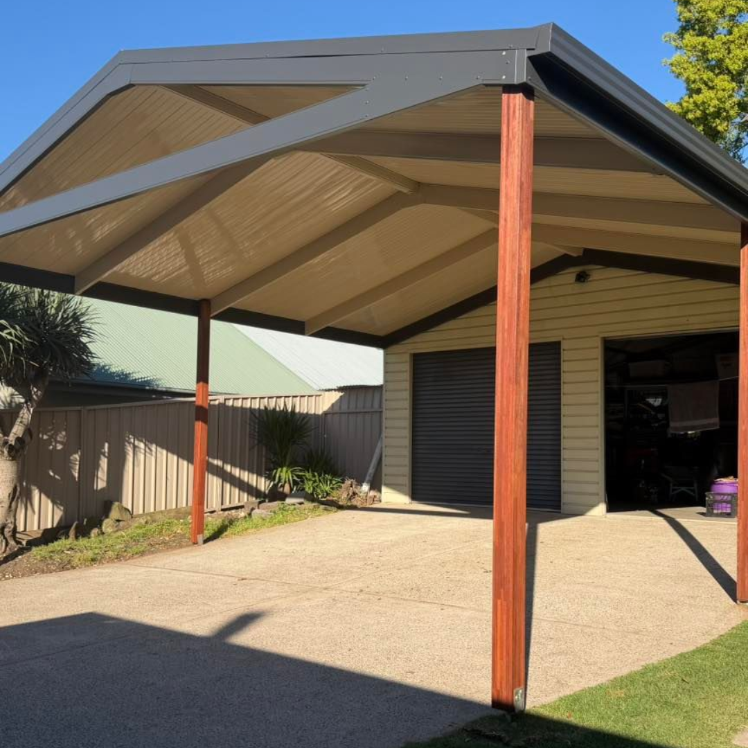 Covered carport with metal roof and wooden posts beside a house, over a paved driveway.