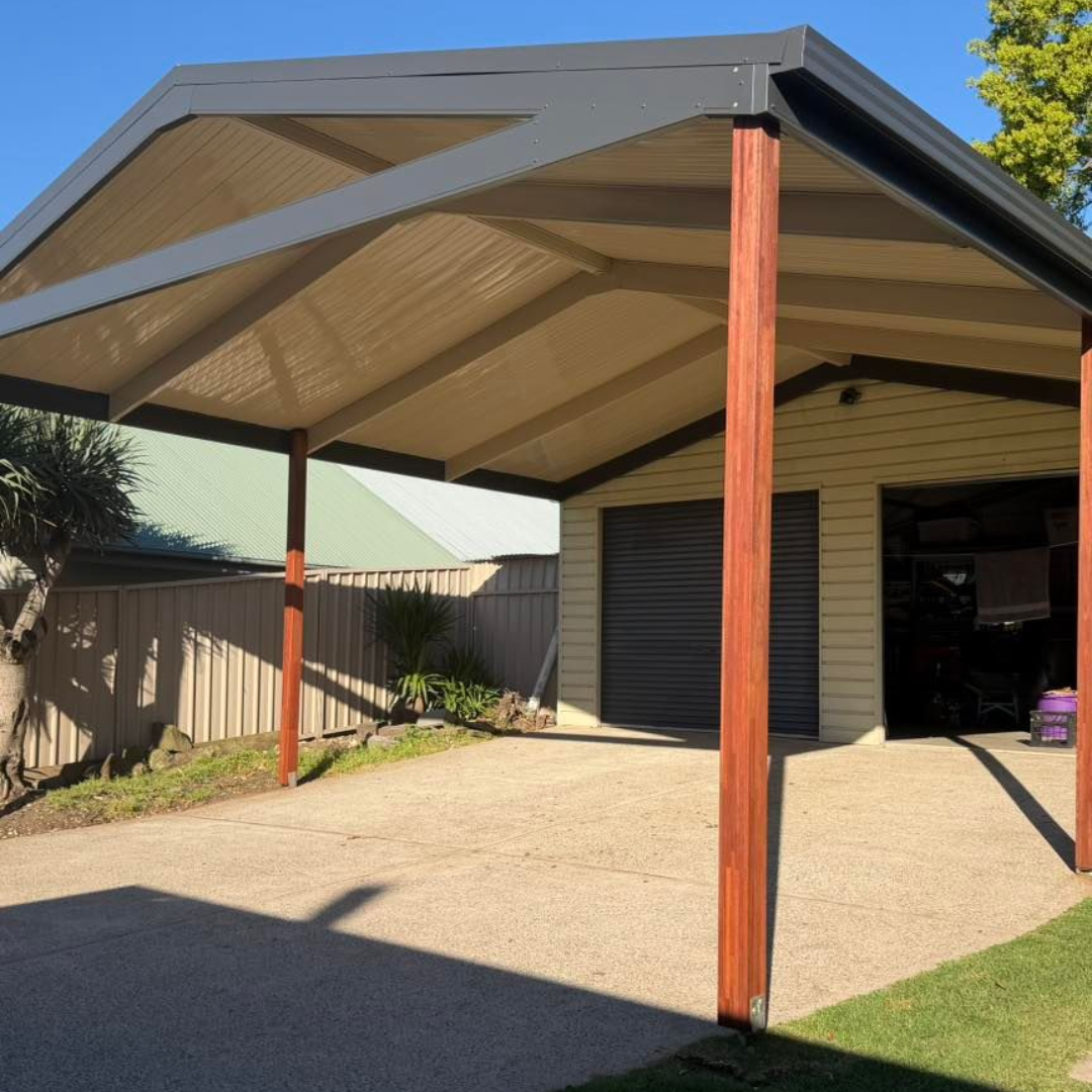Covered carport with timber posts, beige roof, and concrete driveway beside a garage.