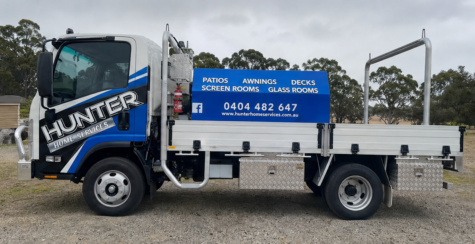 Blue flatbed truck with “HUNTER” branding parked on gravel, side view