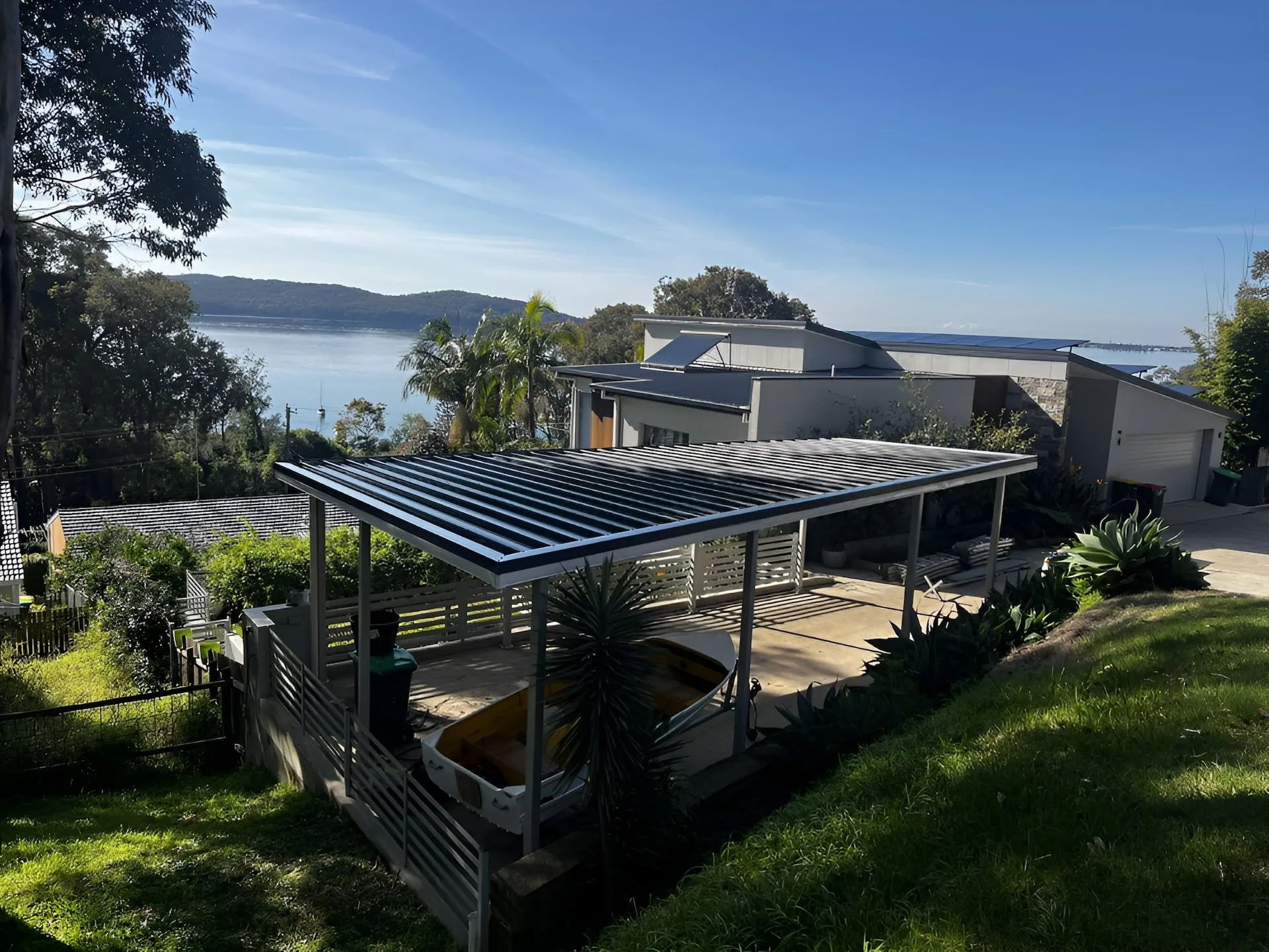 Covered outdoor patio with wooden dining table and chairs beside a modern house under a blue sky