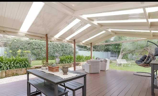 Backyard with green lawn and covered carport, trees in the background, and a truck parked nearby