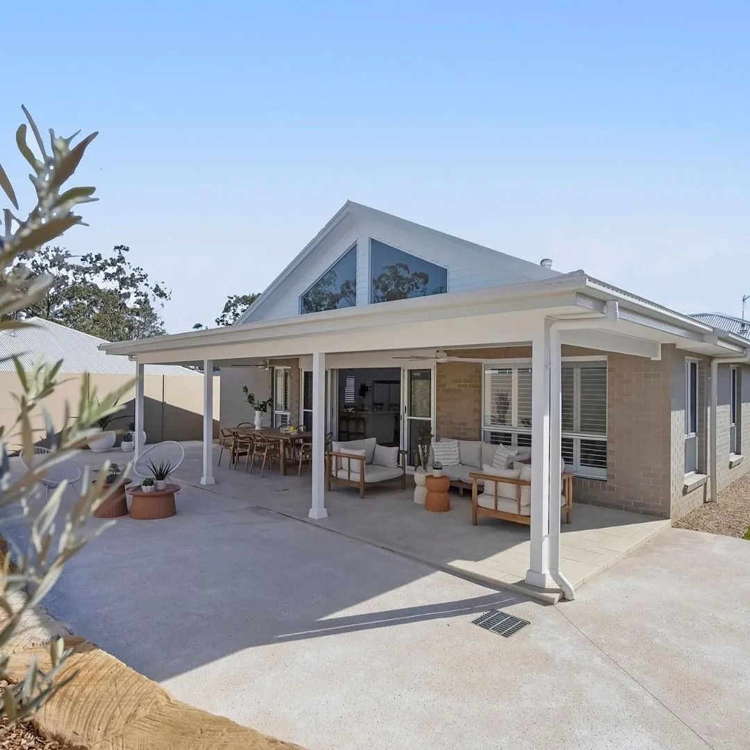 Modern house exterior with a covered patio, white columns, and large windows under a bright blue sky