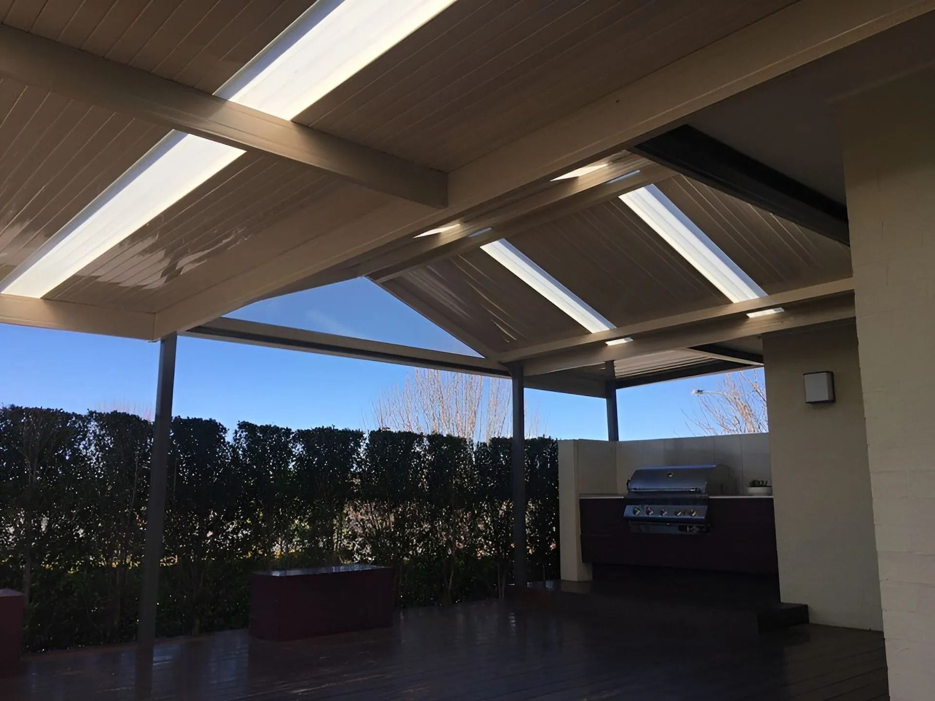 Covered patio with skylight roof, hedge fence, and built-in grill under a blue sky