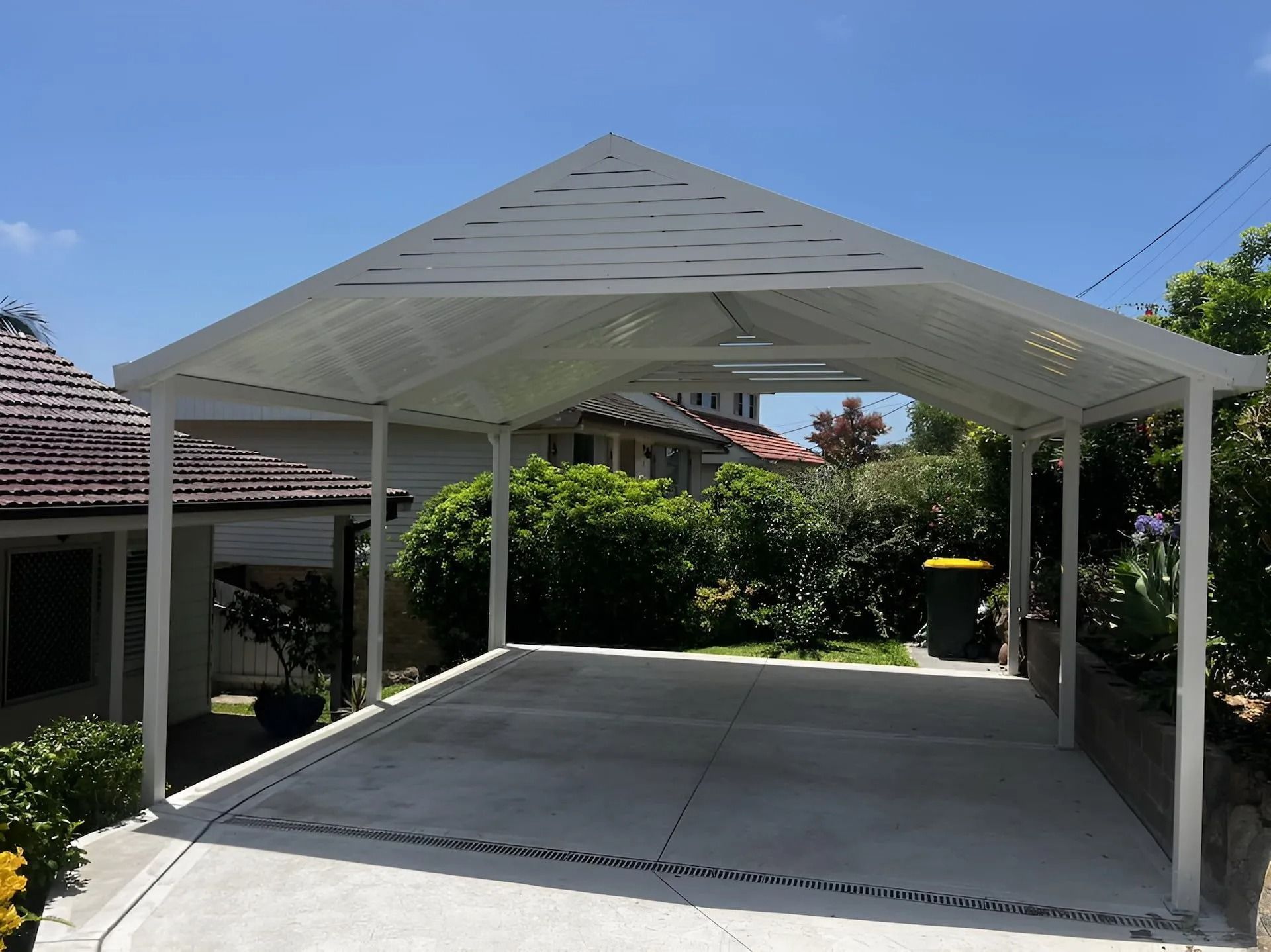 White metal carport with peaked roof over a concrete driveway in a sunny residential yard