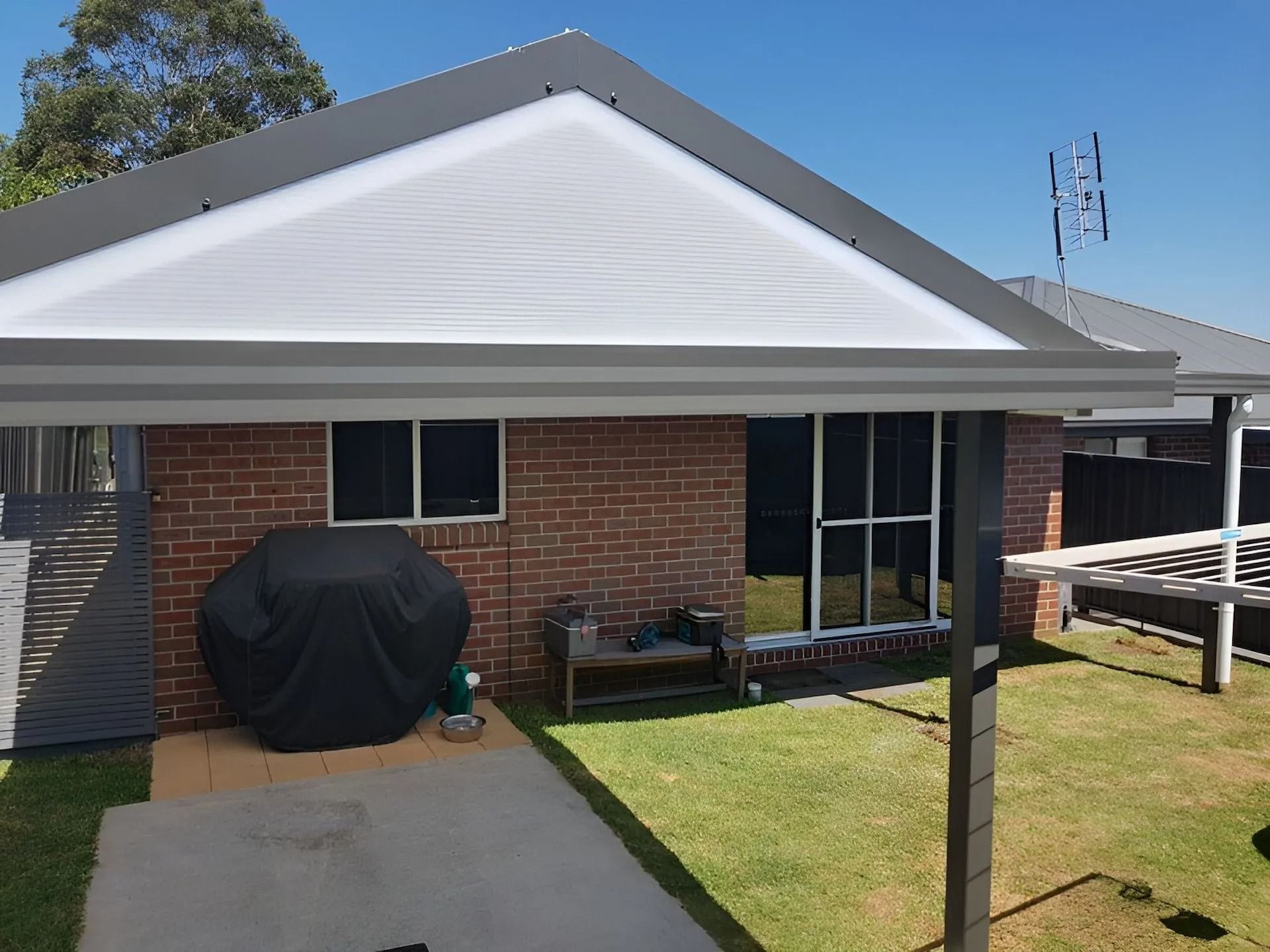 Brick house patio with white gable roof, covered grill, and lawn beside a concrete path