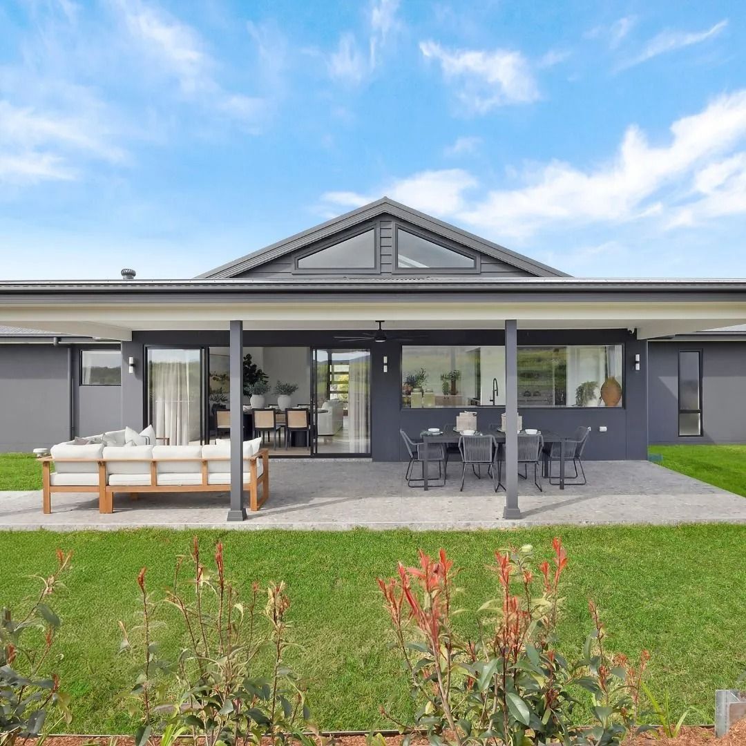Modern gray house with patio seating, gravel terrace, and green lawn under a blue sky
