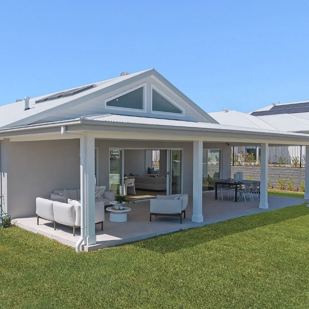 Covered patio with white columns, outdoor seating, and a grassy yard beside a light-colored house