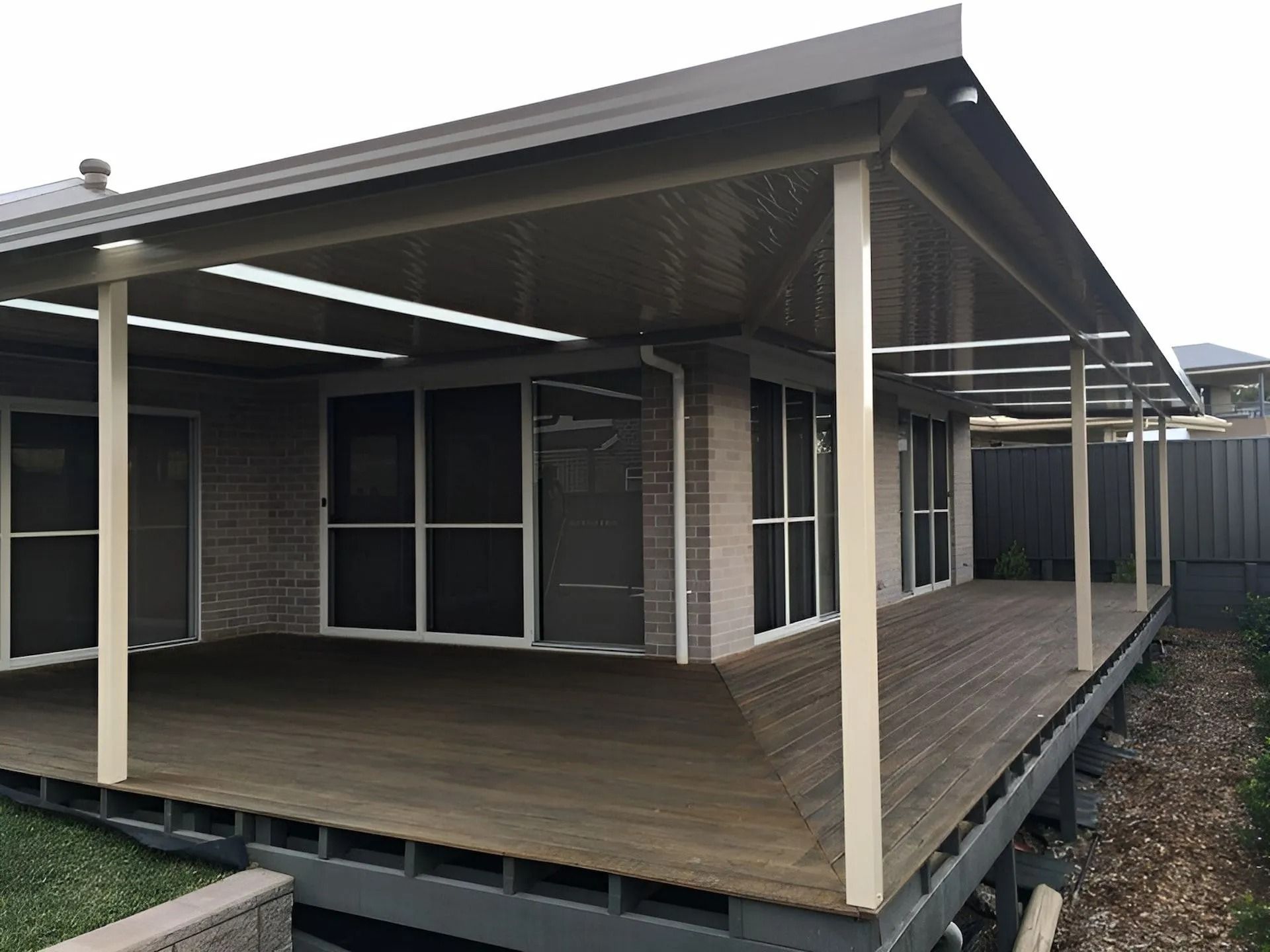 Covered wooden deck outside a modern house with beige posts and large windows