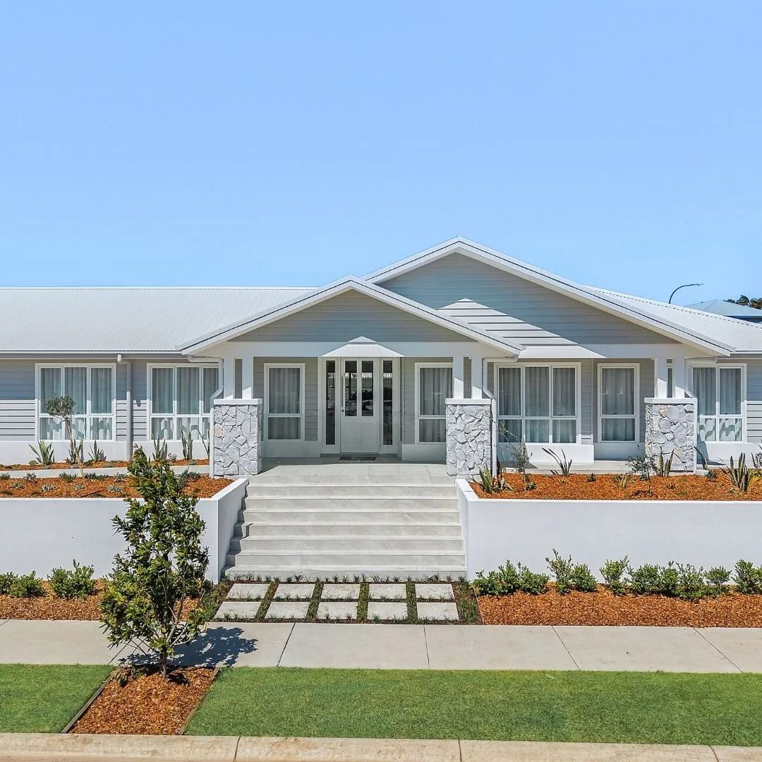 Modern single-story white house with a front porch, central steps, and landscaped lawn under a blue sky