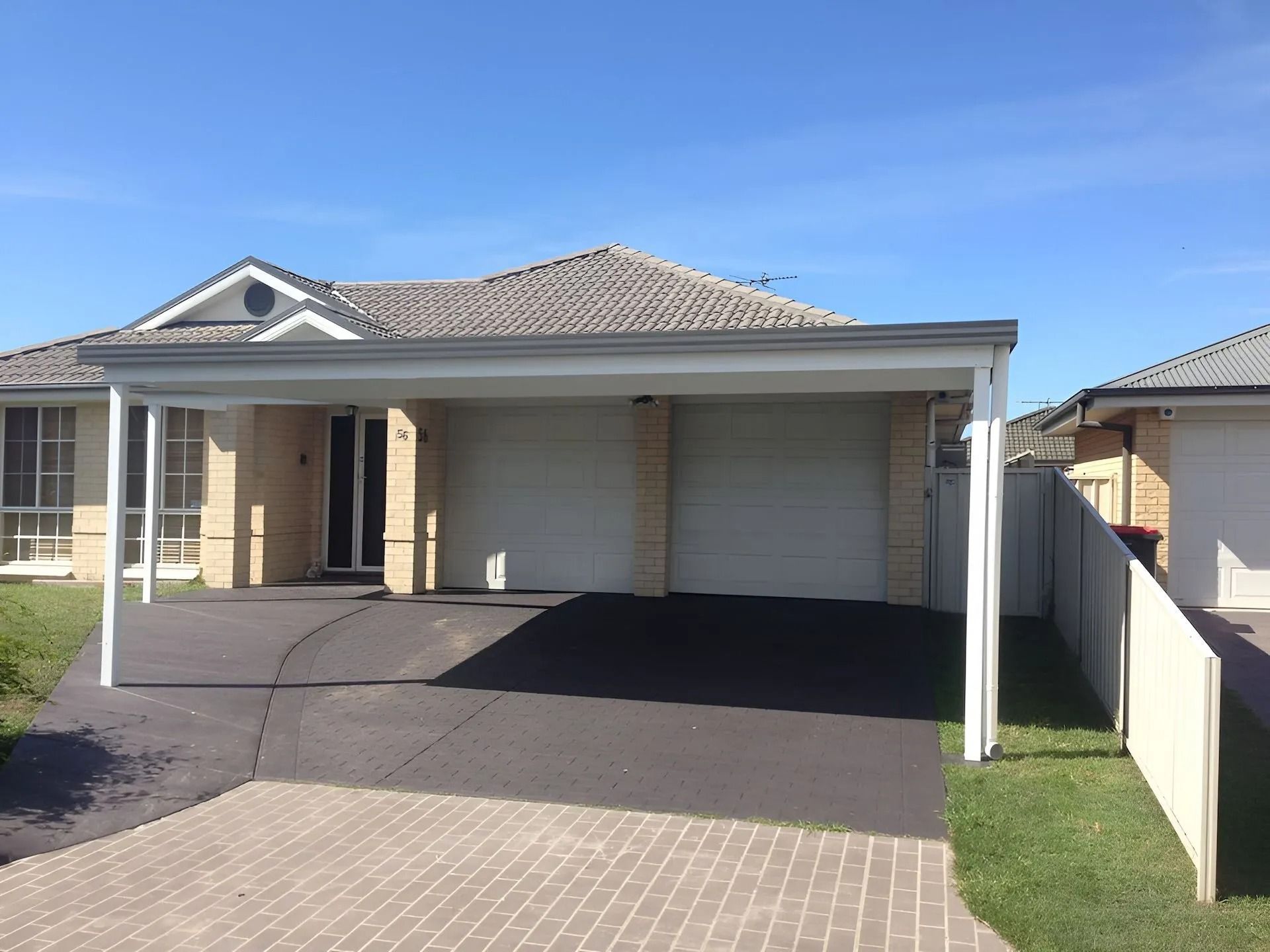 Suburban house with a double garage, driveway, and front lawn under a clear blue sky