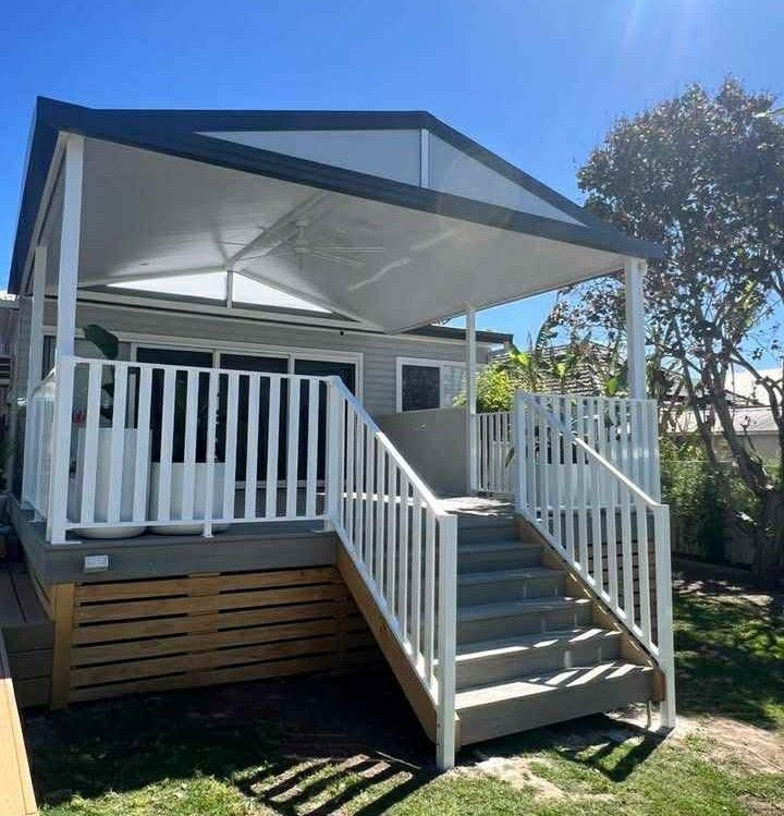 White elevated patio deck with stairs, railings, and a gray canopy in a sunny yard