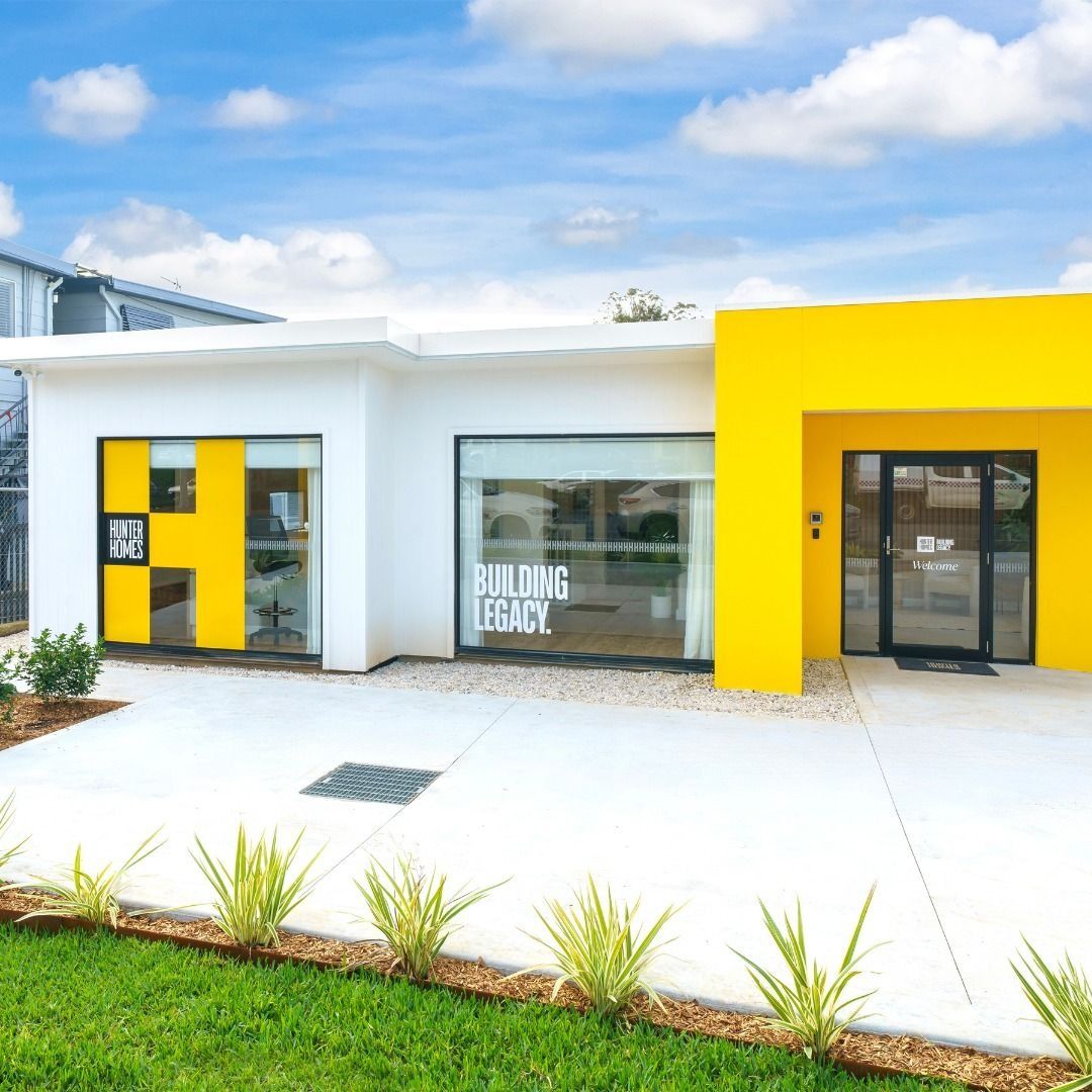 Modern white building with bright yellow accents and glass storefront windows under a blue sky