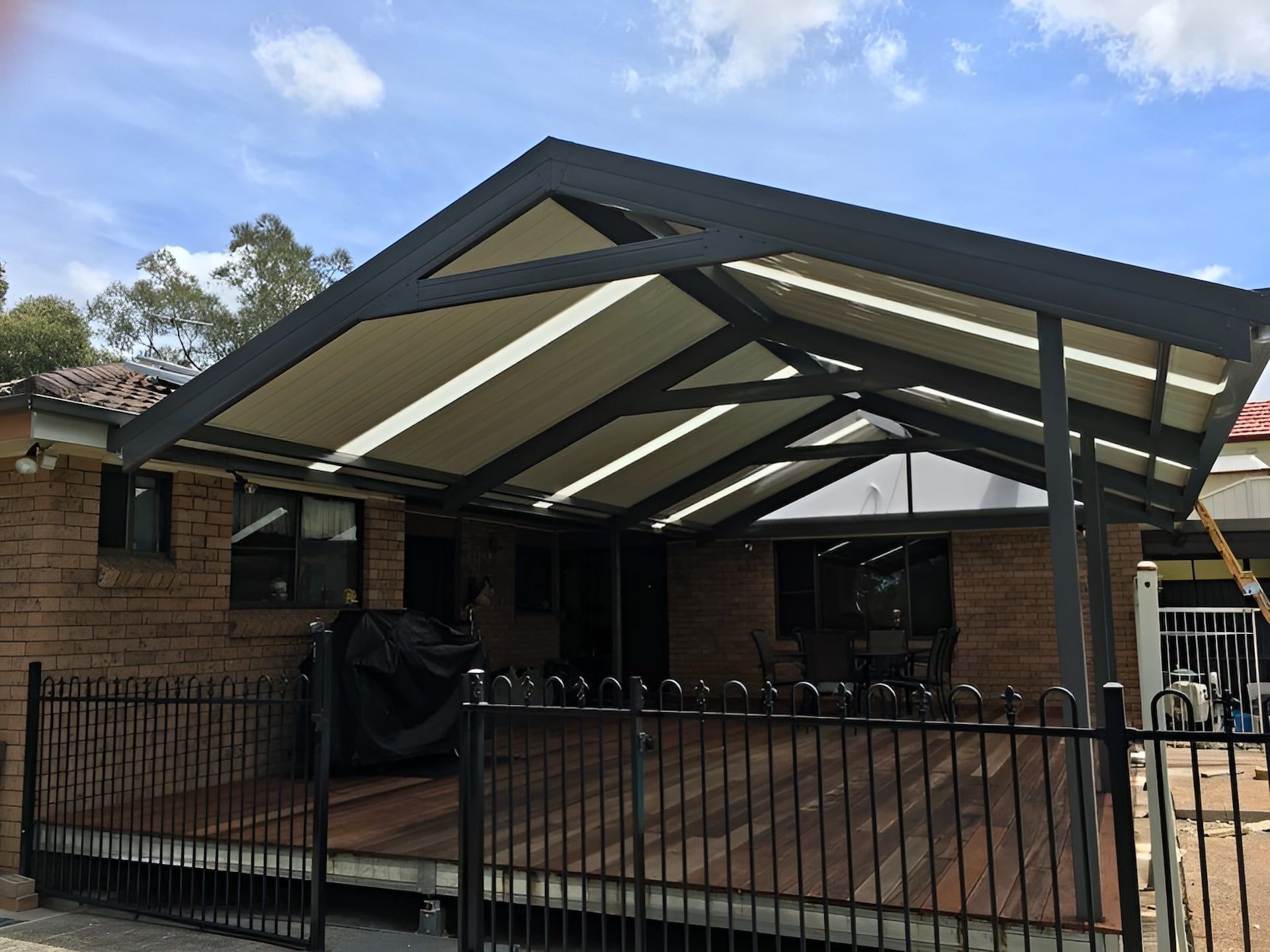 Covered driveway beside brick house with black metal fence and large slanted roof.