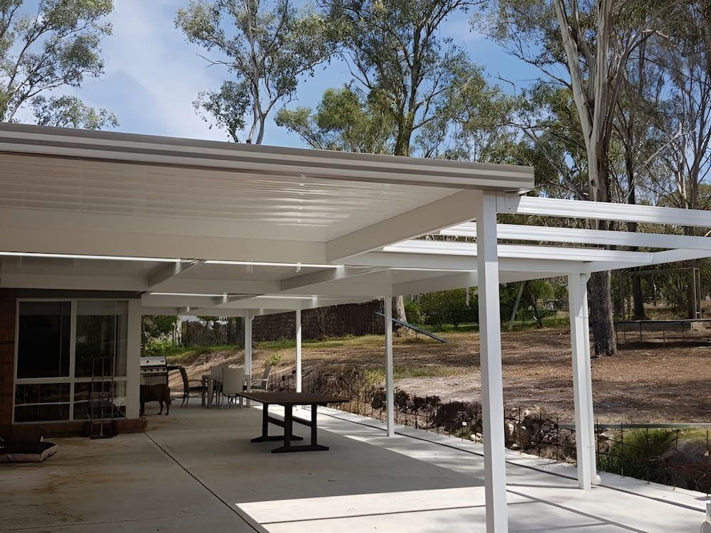 Covered patio with white pergola beams, a picnic table, and trees in the background.