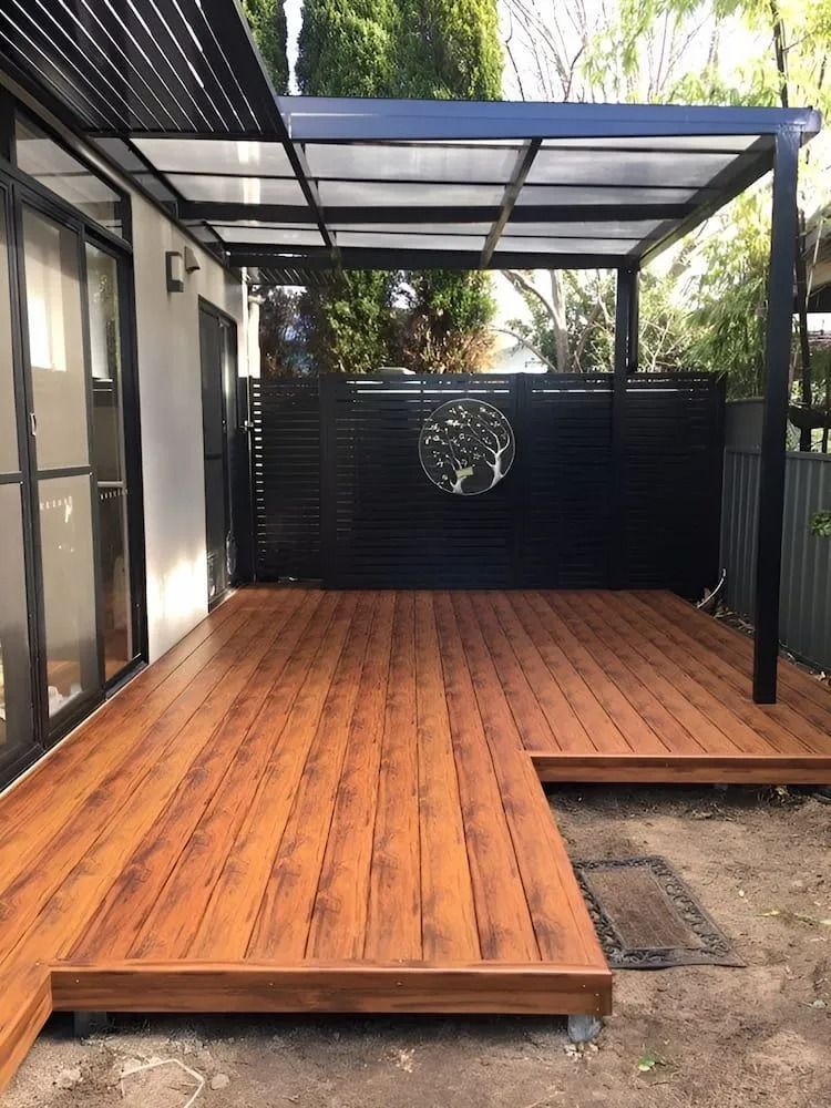 Wooden deck patio with black pergola, sliding glass doors, and privacy screen at the back