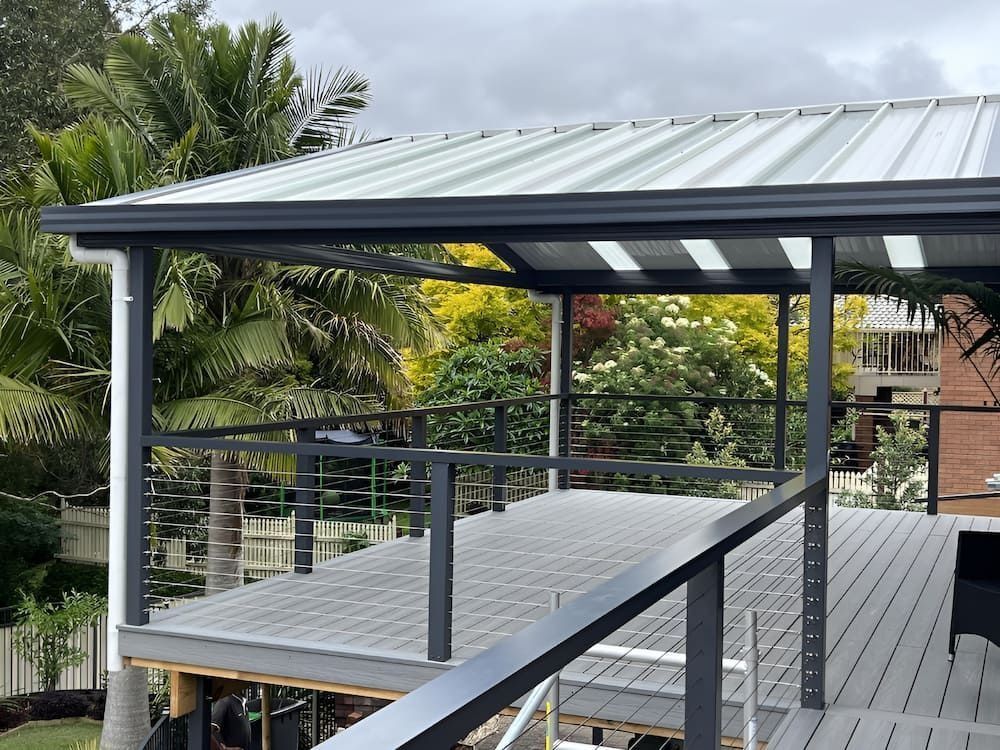 Covered wooden deck with metal roof, railing, and lush tropical greenery beyond
