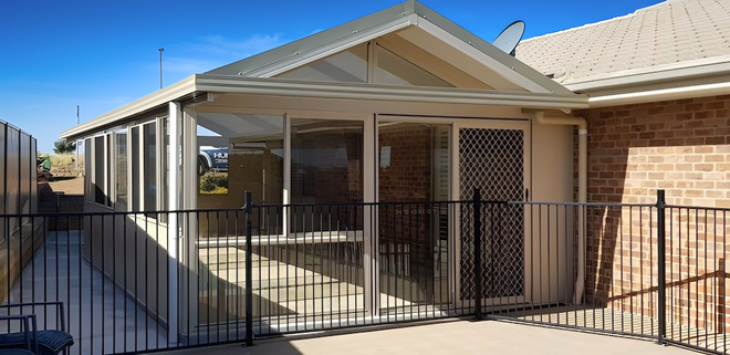 Single-story brick house with covered porch and metal fence under a clear blue sky