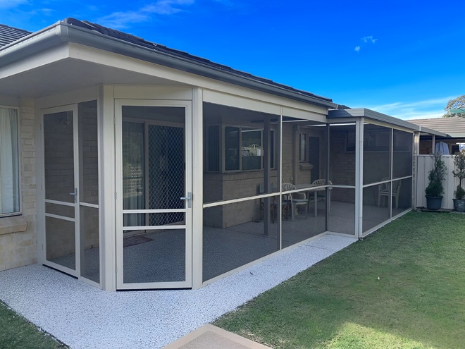 Screened patio beside a beige house with a white roof and grass yard.