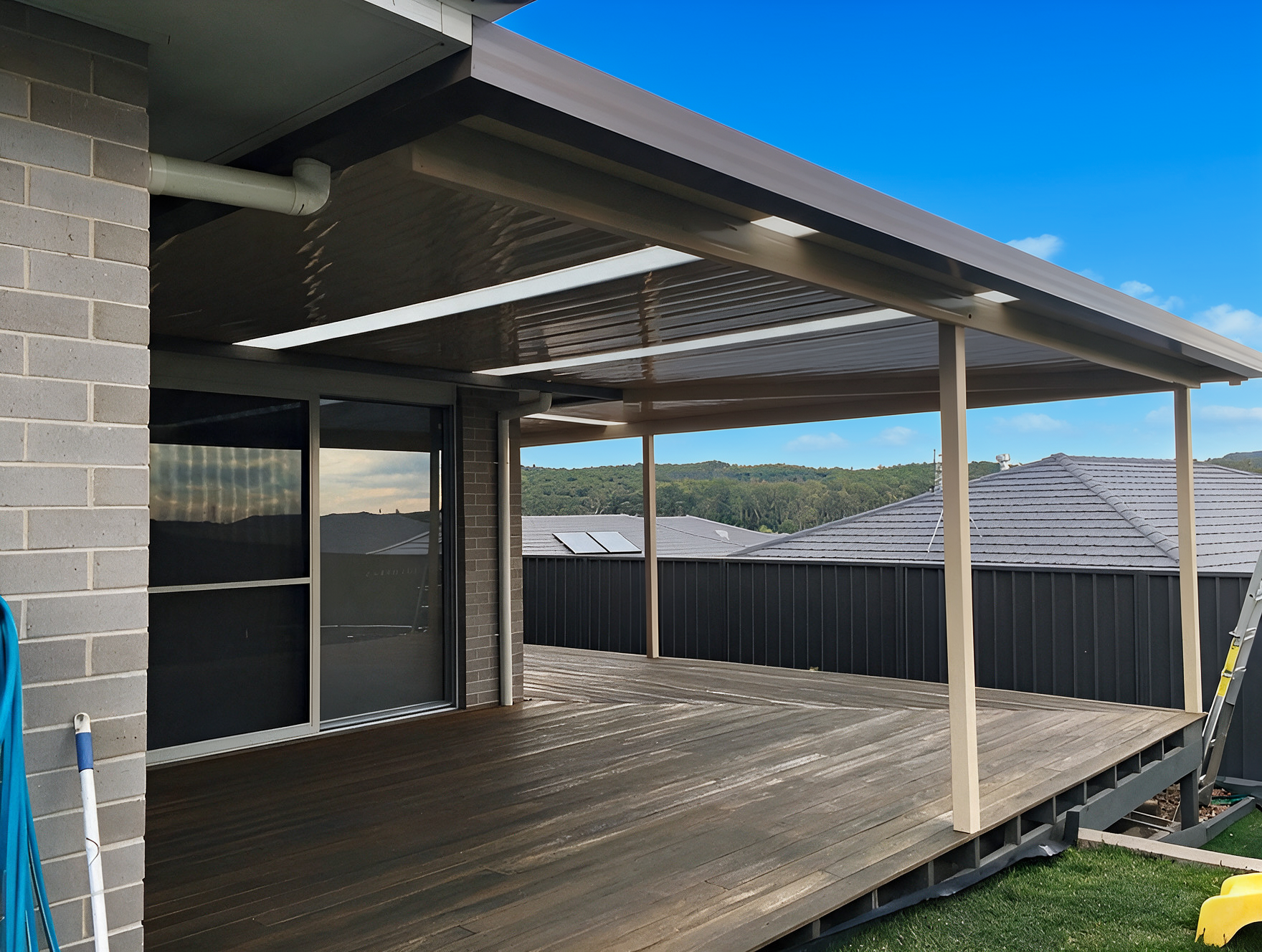 Covered wooden deck with a roof, railings, and sliding glass doors beside a brick house.