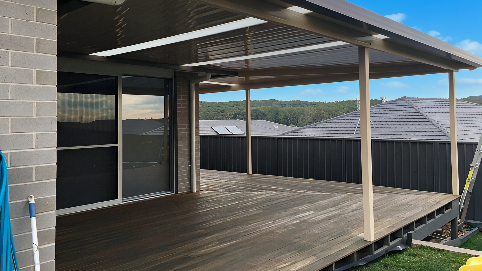 Covered wooden deck with black fence, sliding glass door, and distant hills under blue sky