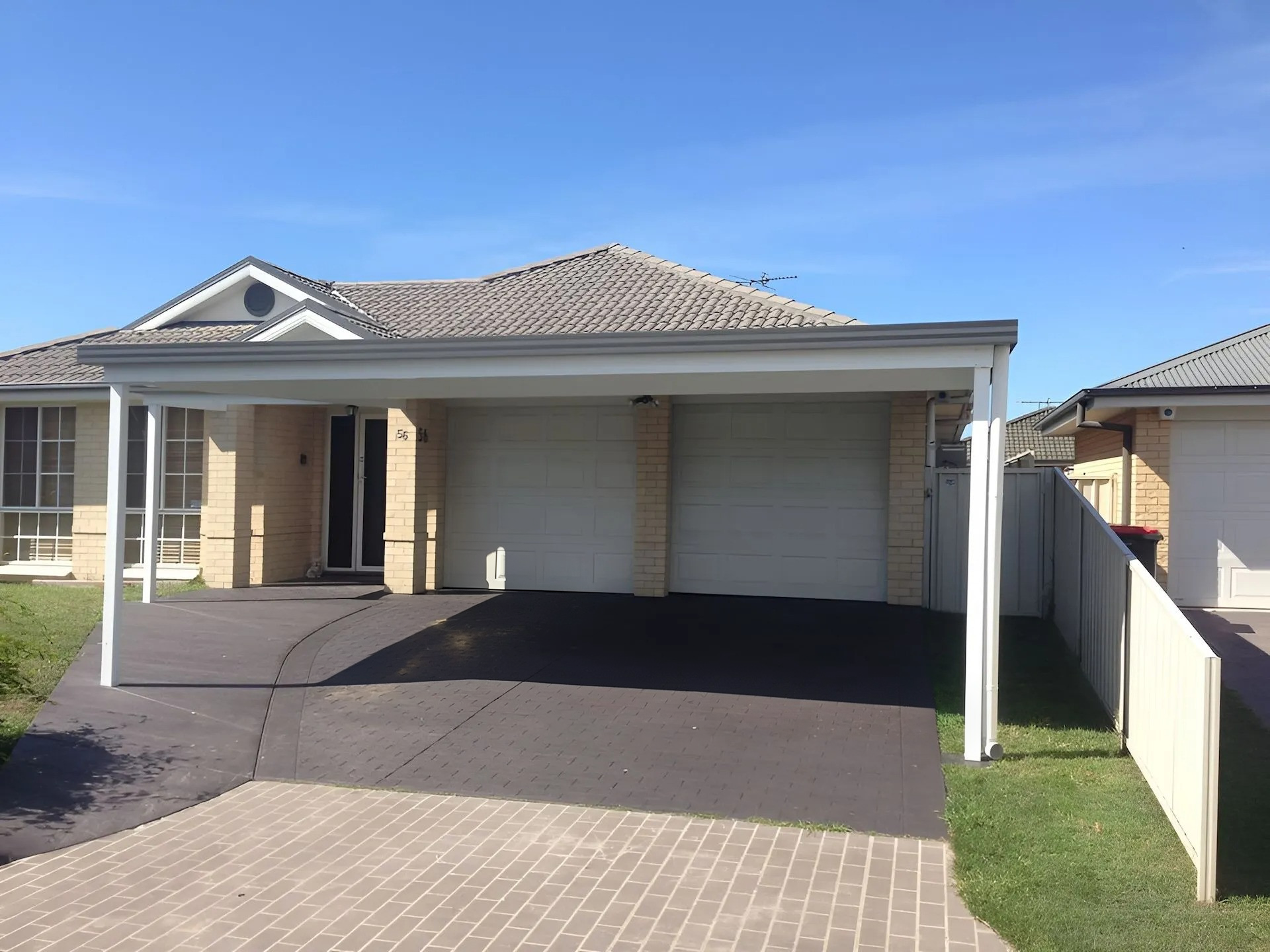 Single-story house with a double garage, driveway, and front lawn under a clear blue sky