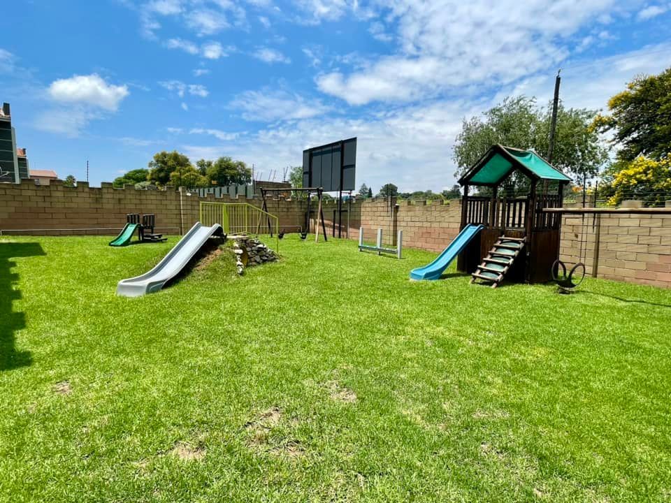 A playground with a slide , swings , and a basketball hoop.
