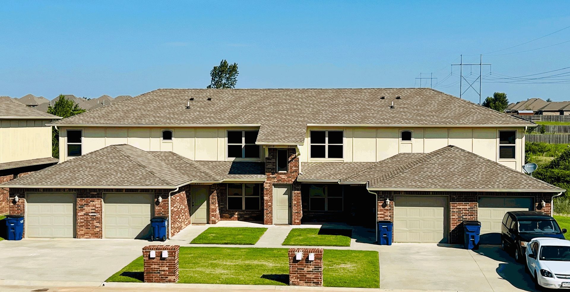 Row of beige townhouses with brown roofs and two parked cars in a sunny residential complex