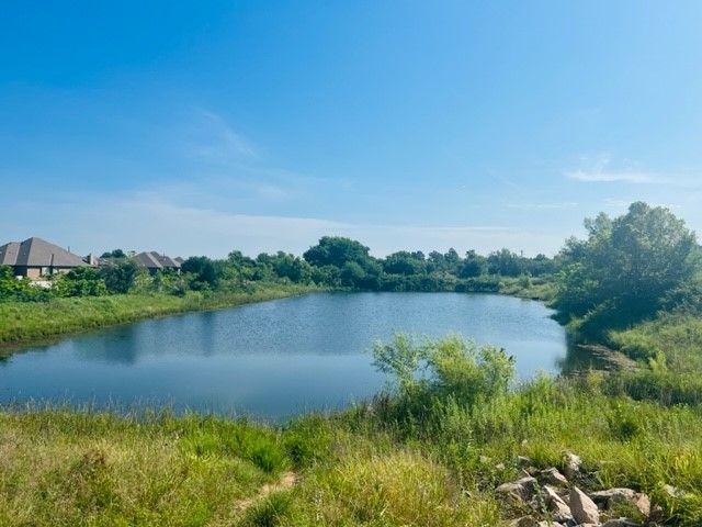 Serene pond under a clear blue sky, with green shoreline and houses in the distance.