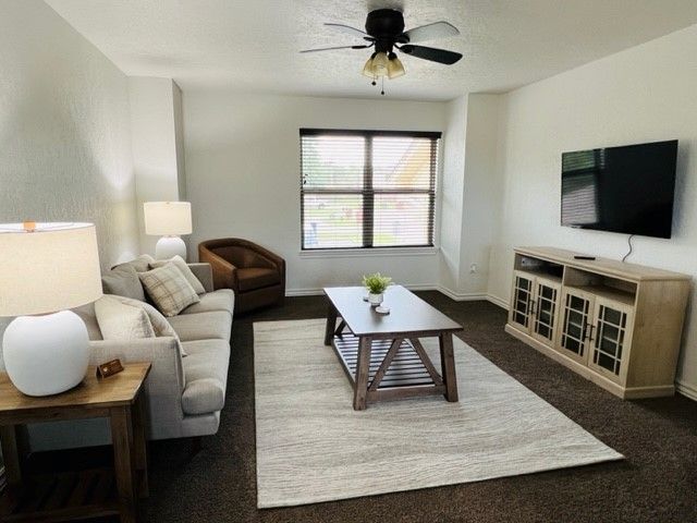 Bright living room with gray sofa, wall-mounted TV, coffee table, and large window with blinds