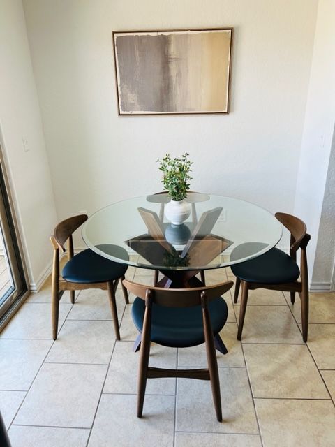 Round glass dining table with four wooden chairs and a small vase centerpiece in a bright tiled corner