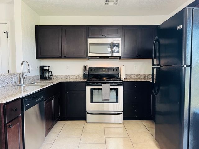 Modern kitchen with dark cabinets, stainless appliances, granite counters, and beige tile floor