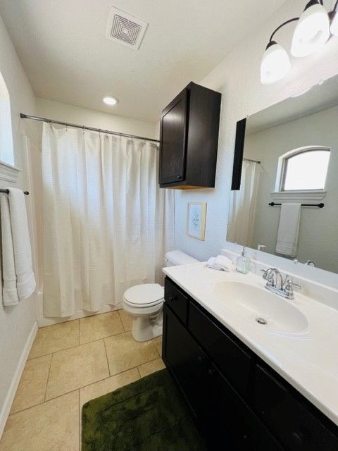 Small bathroom with white shower curtain, dark vanity, green rug, and beige tile floor.