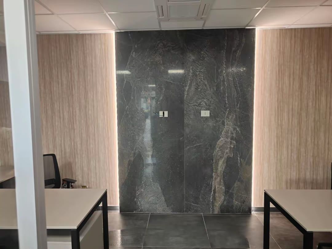 Sala relax vuota in ufficio con scrivanie nere, pareti rivestite in legno e una parete decorativa in marmo scuro.