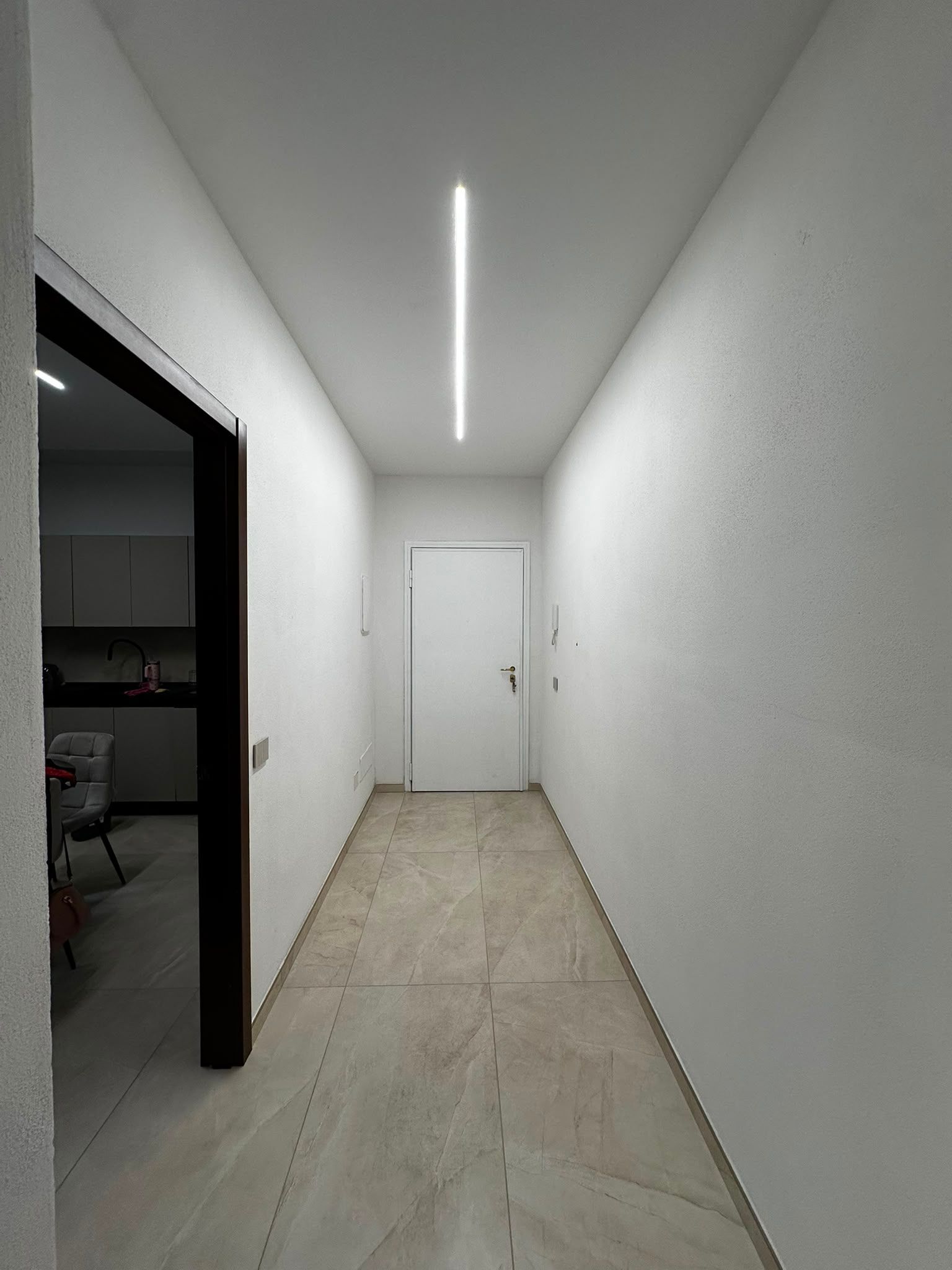 Stretto corridoio bianco con una lampada a soffitto centrale e una porta chiusa in fondo.