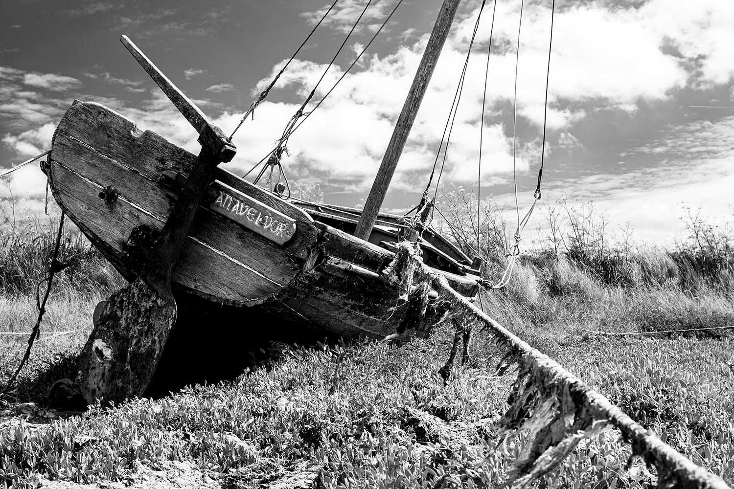 Een oude, verweerde boot ligt aangespoeld op een grashelling onder een bewolkte hemel.