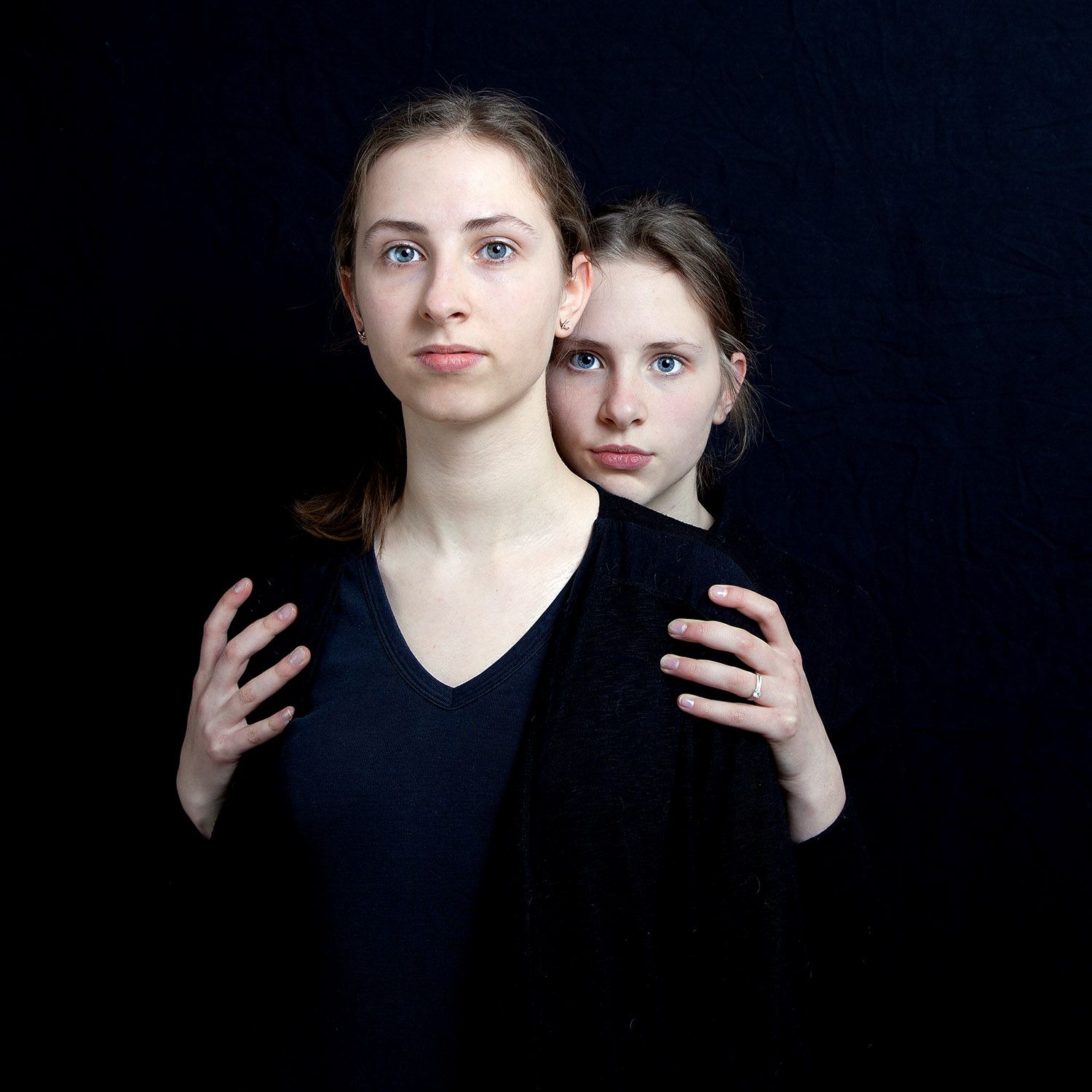 Twee vrouwen tegen een zwarte achtergrond. De ene staat vooraan met haar handen op de schouders van de andere.