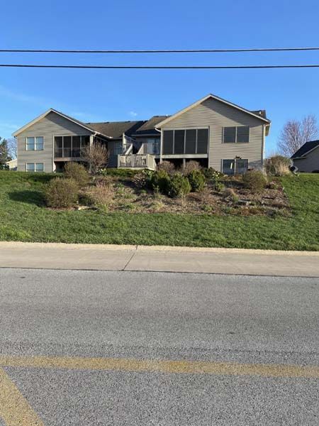 A large house is sitting on top of a grassy hill next to a road.