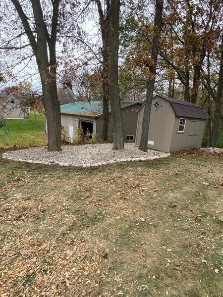 A shed and a garage are in a backyard surrounded by trees.