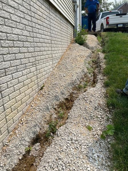 A man is standing next to a brick wall next to a gravel path.