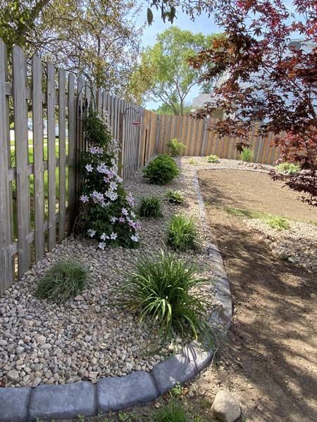 A gravel path leading to a wooden fence with flowers and plants.