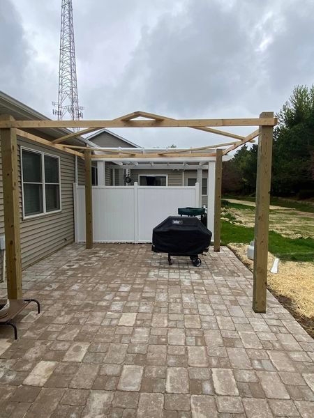A patio with a grill and a pergola in front of a house.